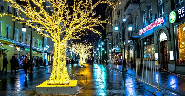 A vibrant city street at night, adorned with dazzling illuminated trees, creating a festive urban atmosphere.