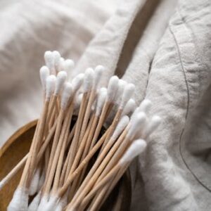 Aesthetic capture of bamboo cotton swabs in a wooden bowl against organic fabric background.